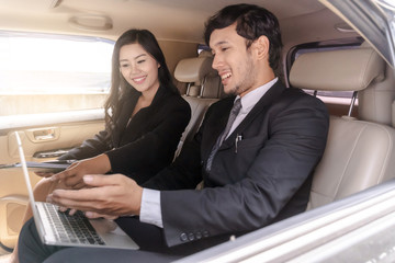 handsome businessman and Business woman sitting in luxury limousine car, working on laptop computer, Works anytime and anywhere concept.