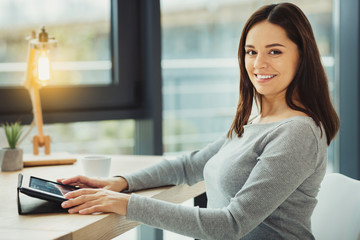 Obraz premium Confident smile. Pretty young qualified HR manager smiling and feeling glad while sitting with a modern tablet