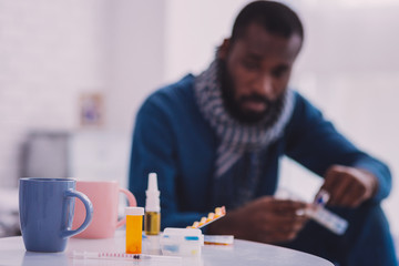 It is mine. Thoughtful dark-skinned man sitting on the bed and looking at medicine