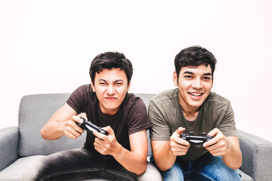 Two Friends Sitting On Sofa And Enjoying Play Video Game Together At Home