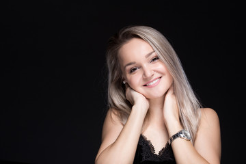 Close up studio portrait of a pretty blonde woman, smiling with and looking at the camera, against plain studio background