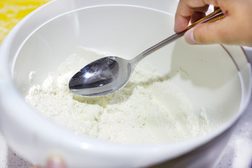 Hand puts the flour by spoon in a white bowl