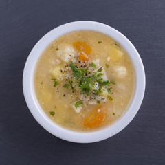 Fresh vegetable soup made of carrot, potato, cauliflower, parsley and rice in white plate,