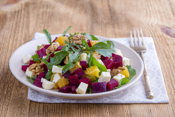 Healthy vegetarian salad with beetroot, green arugula, orange, feta cheese and walnuts on plate