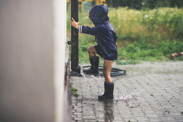Obraz na płótnie Canvas Little girl playing alone outside in bad weather. Summer rain
