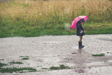 Little girl playing alone outside in bad weather. Summer rain