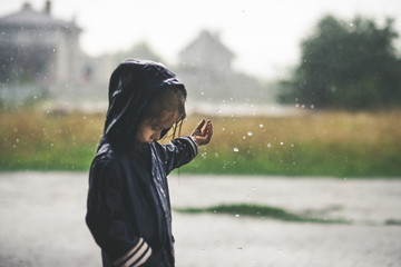 Little girl playing alone outside in bad weather. Summer rain