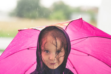 Little girl playing alone outside in bad weather. Summer rain