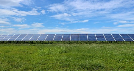Long row of solar panels in a meadow, between green grass and clouds moving in the sky