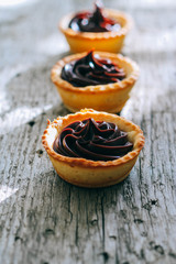 Ruddy tartlets made of shortcake with chocolate ganache on a wooden background