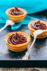 Ruddy tartlets made of short pastry with chocolate ganache on a metal tray