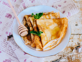 Crepes, thin pancakes with honey and mint on a white plate. Wooden background.