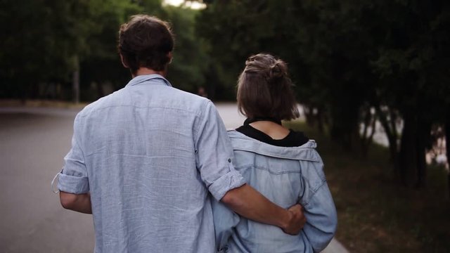 Traking footage of a young couple both in blue similar shirts are walking bonding by park. Romance, calmness, dating. Slow motion