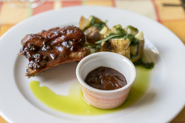 Close up Gourmet Grilled Pork Rib and baked potato Wedges on White Plate with Sauce and Veggies.