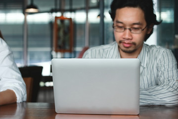 Selective focus on laptop with Asian man on background.