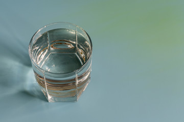 Glass with clear water on a blue background. copy space. Sun rays. toned