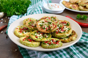 Fried circles of young zucchini with garlic, red pepper, greens on a plate. Vegetarian menu. Close up