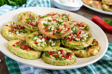Fried circles of young zucchini with garlic, red pepper, greens on a plate. Vegetarian menu. Close up
