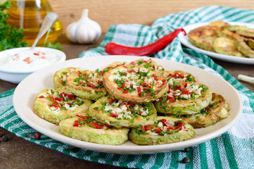 Fried circles of young zucchini with garlic, red pepper, greens on a plate. Vegetarian menu.