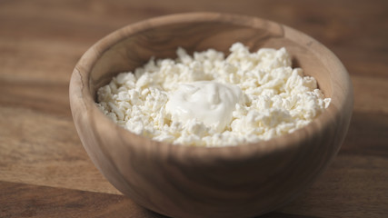 closeup sour cream pour on cottage cheese in wood bowl