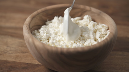 closeup sour cream pour on cottage cheese in wood bowl