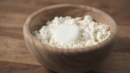 closeup sour cream pour on cottage cheese in wood bowl