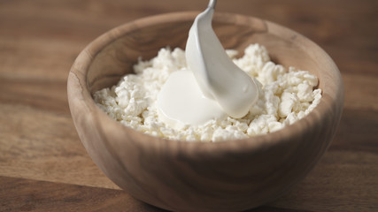 closeup sour cream pour on cottage cheese in wood bowl