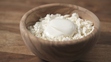 closeup sour cream pour on cottage cheese in wood bowl