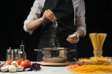 The chef prepares spaghetti and pasta, salt water, against a dark background, the concept of cooking