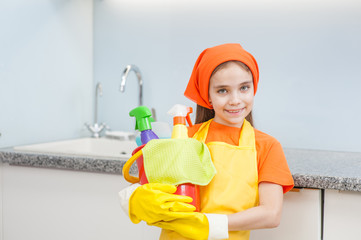 Happy little girl with cleaning supplies in bucket at kitchen