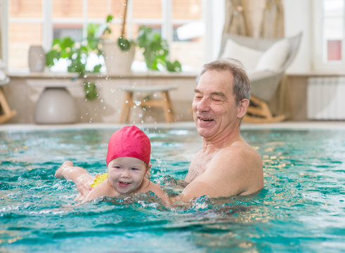 Grandfather  teaches to swim his little granddaughter in the pool
