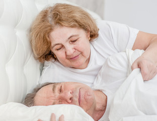 Senior woman cares about her husband, covers him with a blanket