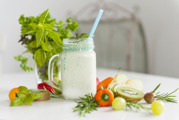Fresh smoothies on a table with bright vegetables and a bunch of green herbs close up