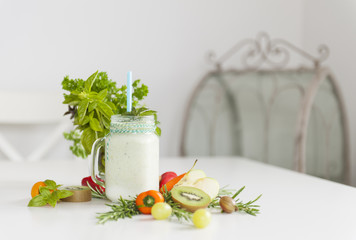 Fresh smoothies on a table with bright vegetables and a bunch of green herbs