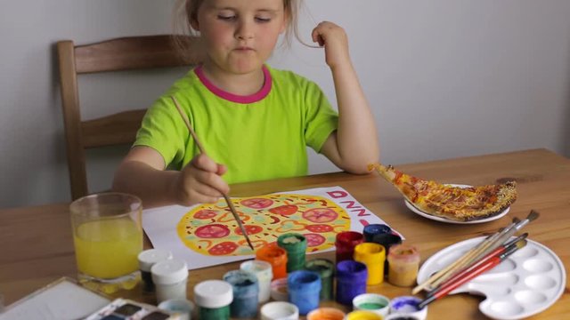 Child draws a big pizza sitting at the table at home