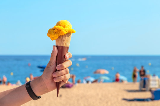 mango-flavored ice cream in a waffle cone in the hand of a teenager against the beach and the sea