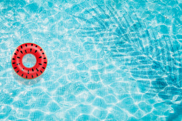 Fototapeta na wymiar Pool float, ring floating in a refreshing blue swimming pool with palm tree leaf shadows in water