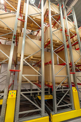 Large cardboard boxes stand on the shelves of a very high metal rack.