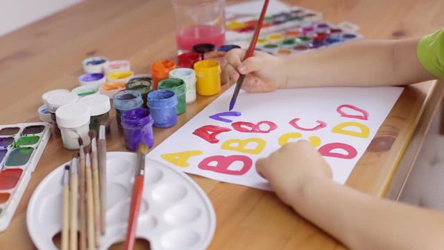 Child writes letters with a brush on a white sheet of paper