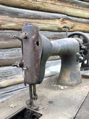 Old sewing machine, with manual drive. Covered with corrosion, dust and cobwebs. Against the background of a wooden abandoned barn.