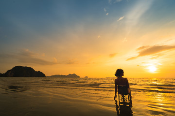 Woman sitting on the beach with beautiful sunset in Trang province, Thailand.