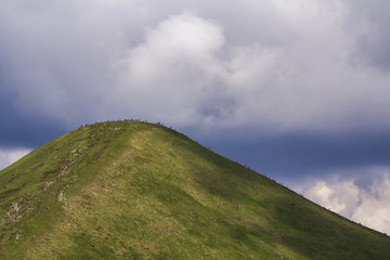 View from afar of lit by summer sun mountain Hoverla with lots of people traveling up and down by...