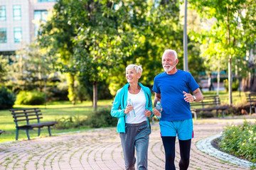 Happy senior couple jogging outdoors in park.