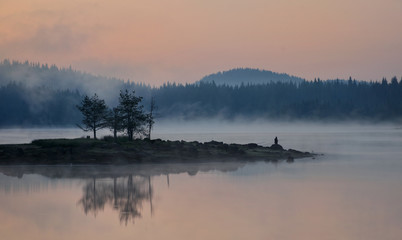 Mist sunrise by the dam lake in Rhodope mountain, Bulgaria.  A man is fishing early in the morning.