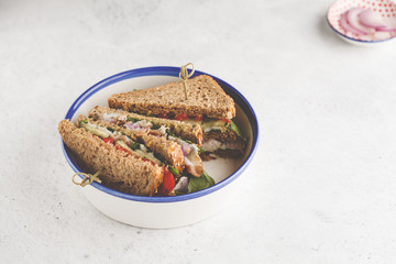 Sandwich with meat and vegetables on a white plate.