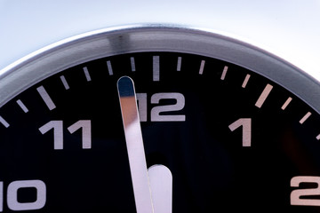 Closeup of modern black chrome clock on white background indicates twelve o'clock, wake up, time for action, time up or midday. Time passing concept for business urgency and running out of time.
