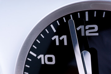 Closeup of modern black chrome clock on white background indicates twelve o'clock, wake up, time for action, time up or midday. Time passing concept for business urgency and running out of time.