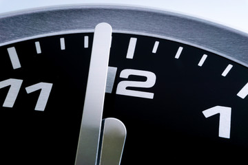 Closeup of modern black chrome clock on white background indicates twelve o'clock, wake up, time for action, time up or midday. Time passing concept for business urgency and running out of time.