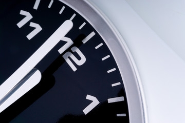 Closeup of modern black chrome clock on white background indicates twelve o'clock, wake up, time for action, time up or midday. Time passing concept for business urgency and running out of time.