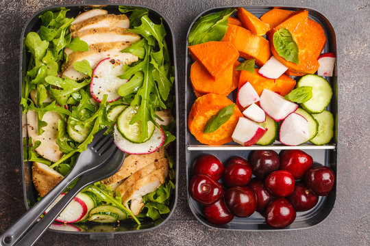 Healthy meal prep containers with grilled chicken with salad, sweet potato, berries, fruits and vegetables. Dark background, top view.